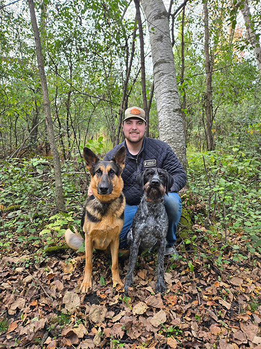 an image of a man crouched in the woods with two dogs